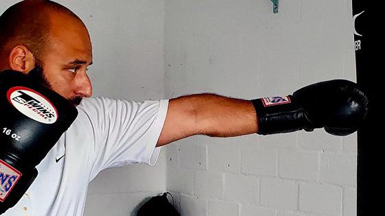 Mann mit schwarzem Boxhandschuh, der einen Schlag auf einen schwarzen Boxsack ausf&uuml;hrt.