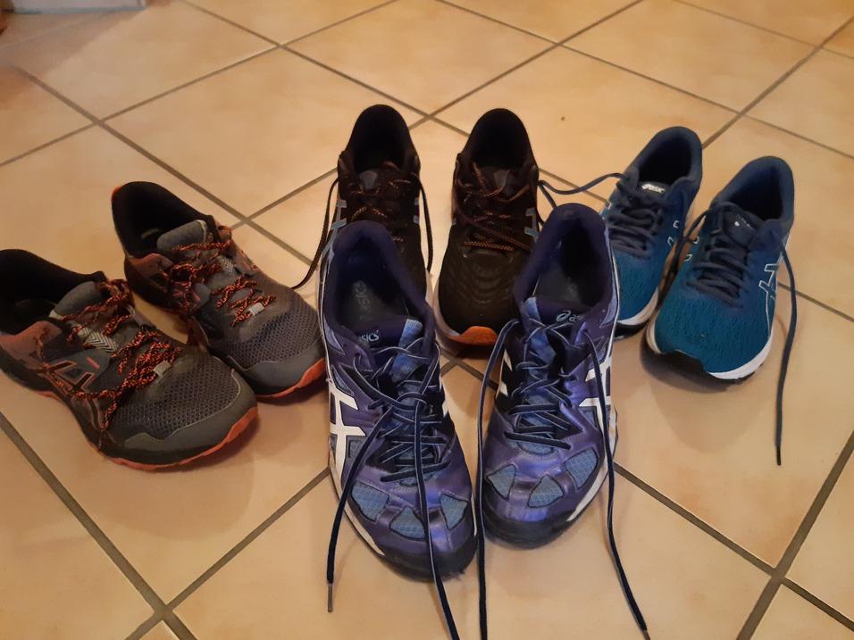 Sechs Paar Laufschuhe in verschiedenen Farben und Designs auf einem gefliesten Boden angeordnet.