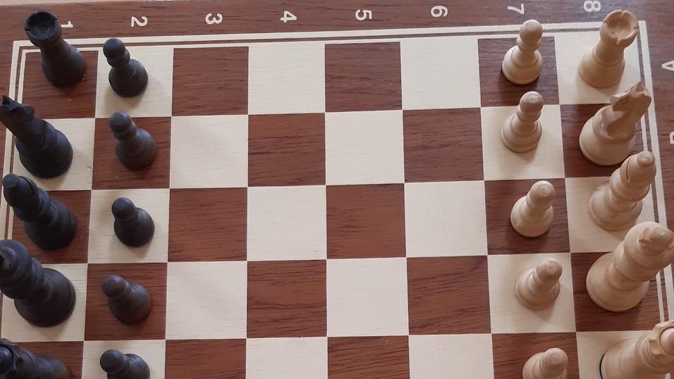 Schachbrett mit schwarzen und wei&szlig;en Figuren, bereit f&uuml;r eine Partie, auf einem hellen Tisch.