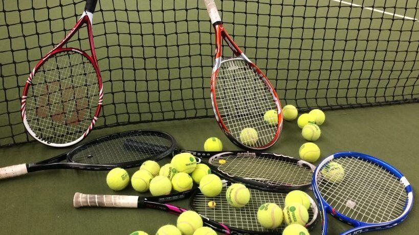 Drei Tennisschl&auml;ger und zahlreiche gelbe Tennisb&auml;lle liegen auf einem Tennisplatz hinter einem Netz.