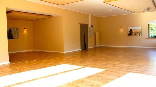 Heller, leerer Raum mit Holzfu&szlig;boden, beige W&auml;nden und einem Fenster, dekoriert mit Bildern und indirekter Beleuchtung.