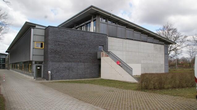 Moderne Geb&auml;ude mit grauer Fassade, Treppe und gro&szlig;en Fenstern, umgeben von Rasen und B&auml;umen.