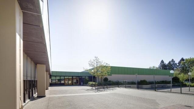 Fassade eines modernen Geb&auml;udes mit gr&uuml;ner Dachfarbe und gepflastertem Vorplatz bei klarem Himmel.