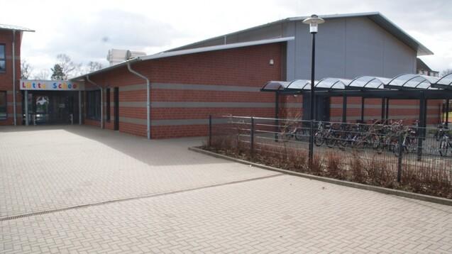 Eingangsbereich einer Schule mit buntem Schriftzug &bdquo;L&uuml;tte School&ldquo; und &uuml;berdachtem Fahrradparkplatz im Hintergrund.