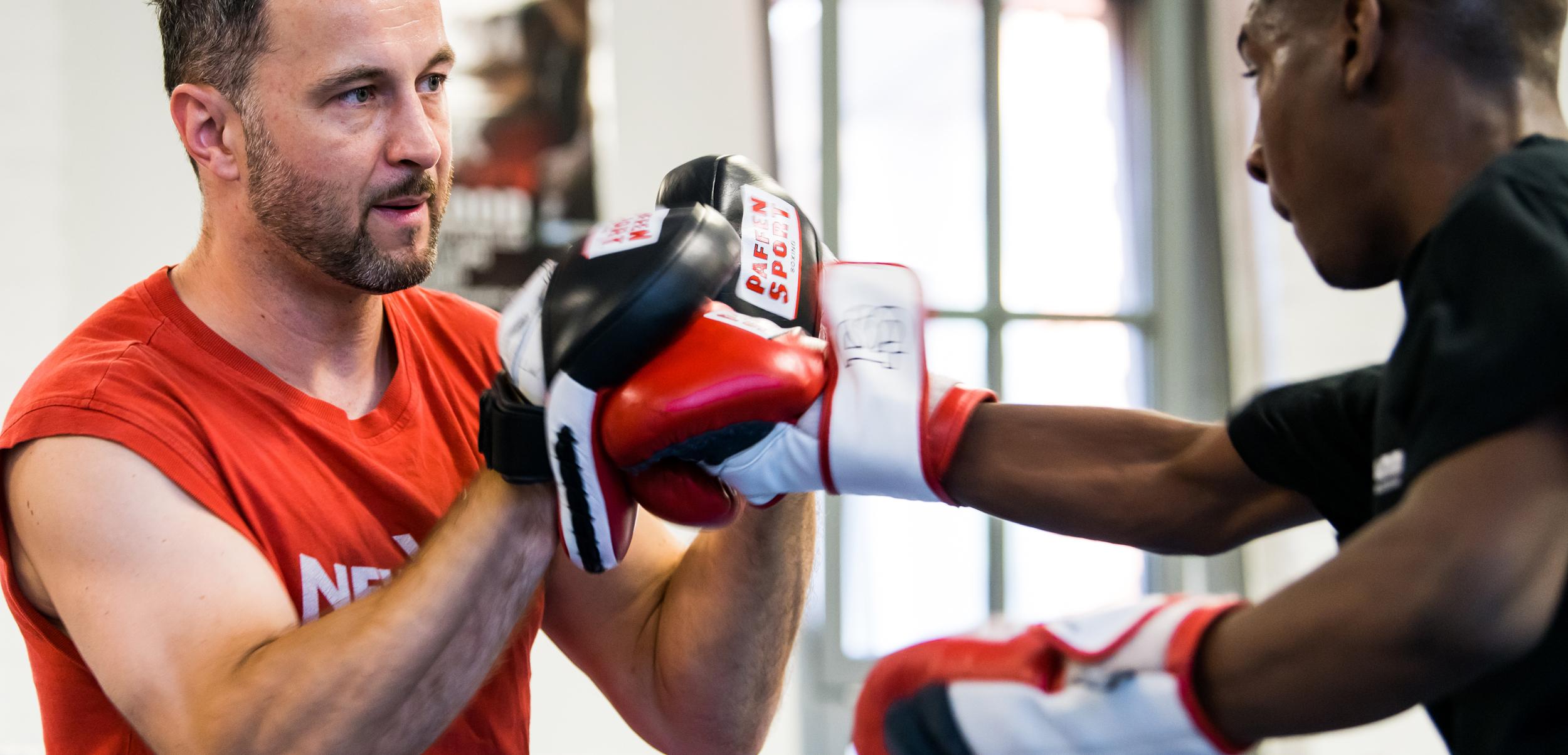 Trainer überwacht das Boxtraining eines Schülers, beide tragen Boxhandschuhe in einem Trainingsraum.