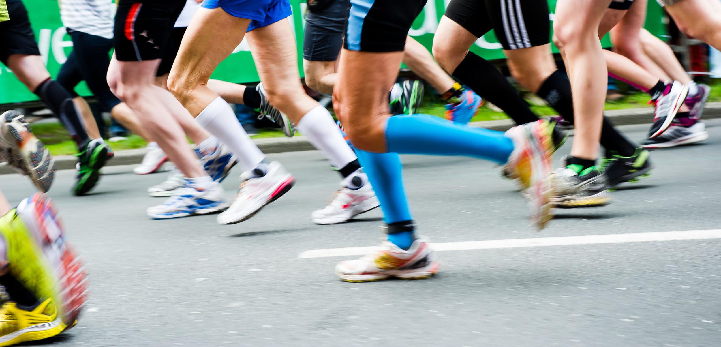 Bunte Laufschuhe rennen in einem Marathon, während Zuschauer im Hintergrund auf der Strecke stehen.
